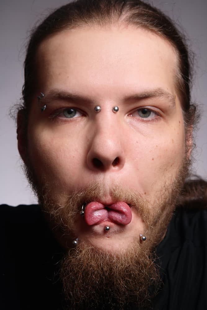  Man with piercings showing his tongue cut in two.