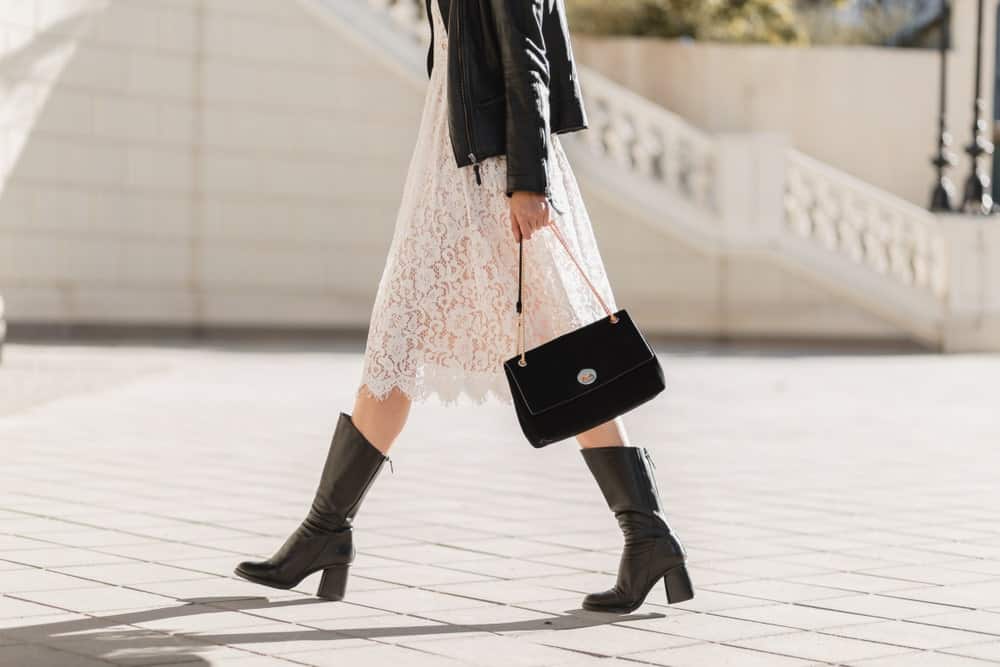 A woman in white lace dress and high leather boots walking on a street.
