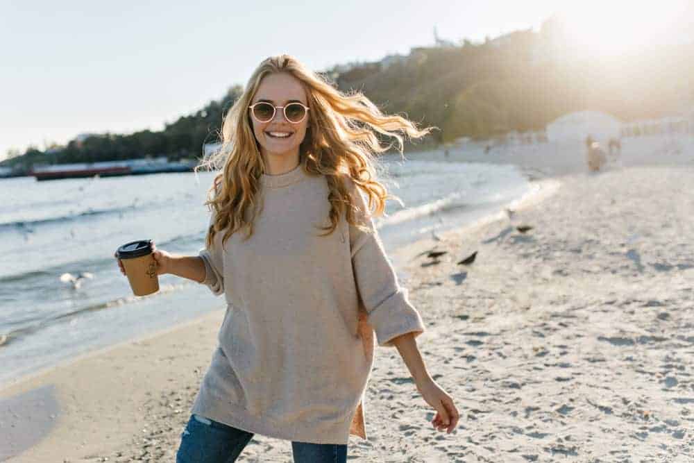Woman in a boyfriend sweater posing near the ocean.