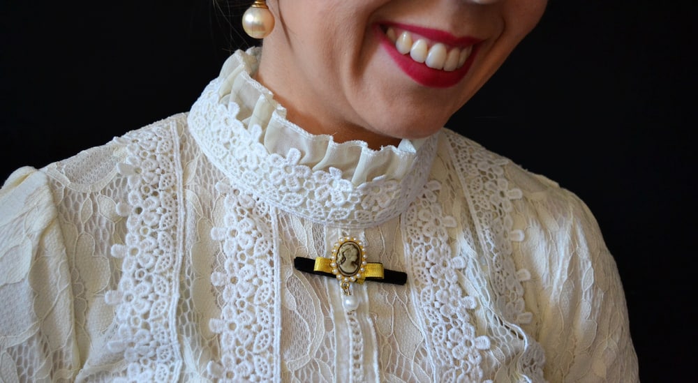 Smiling woman wearing a white lace blouse with cameo-shaped brooch.