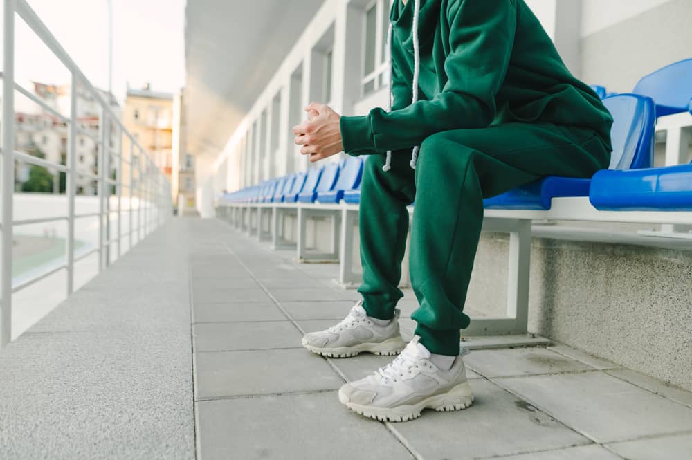 Man in green coordinates and white sneaker sitting on a blue chair.