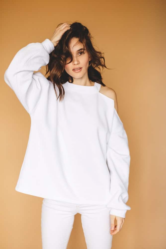 Woman in a white cutout sweater against a beige background.