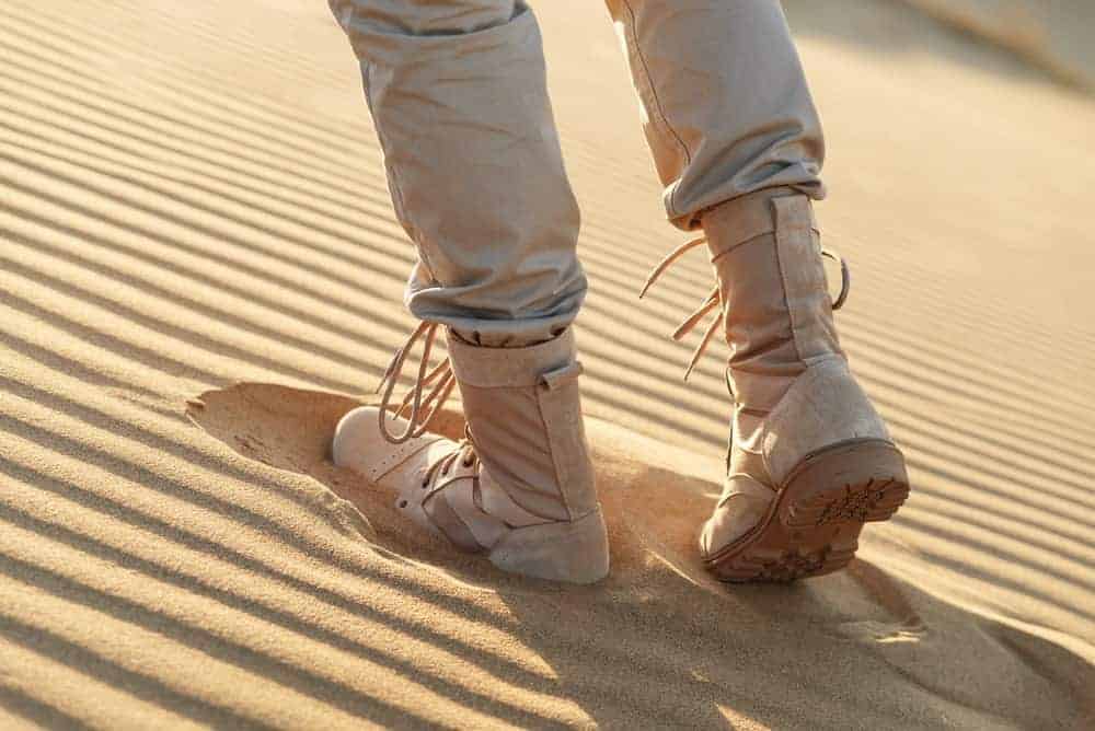 A man in beige boots walking through the desert.
