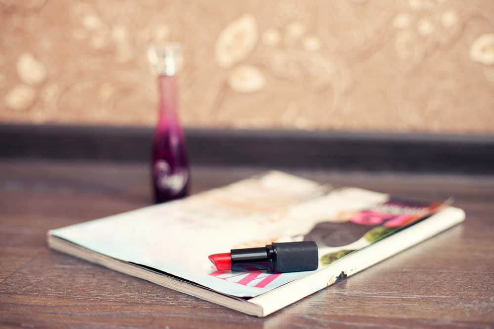 A red lipstick lying on a fashion book on a wooden desk.
