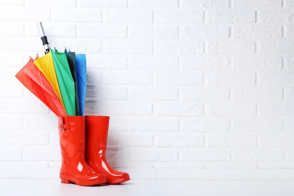 Red galoshes boots with a multicolored umbrella against a brick background.