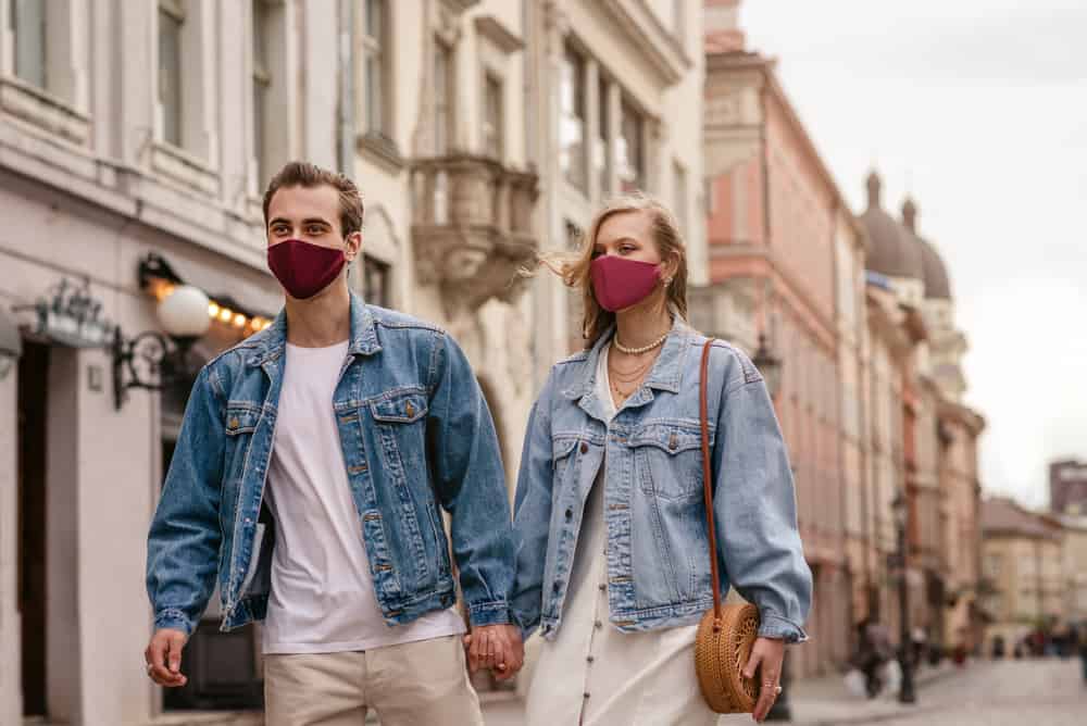 A couple in masks and denim jackets walking down the empty street.