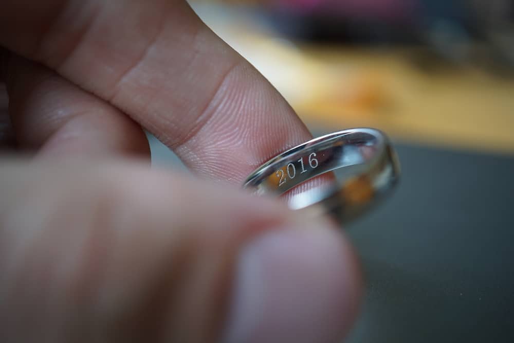 Male hand holding a wedding ring with an engraved year, 2016.