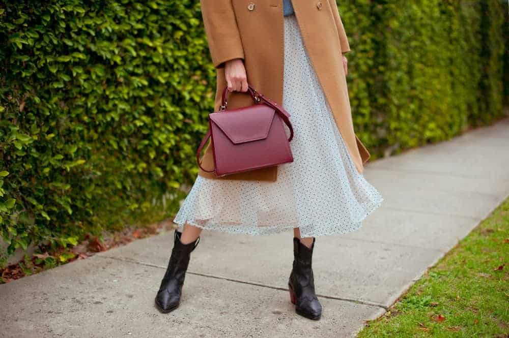 Woman in boots and tulle midi skirt holding a burgundy bag.
