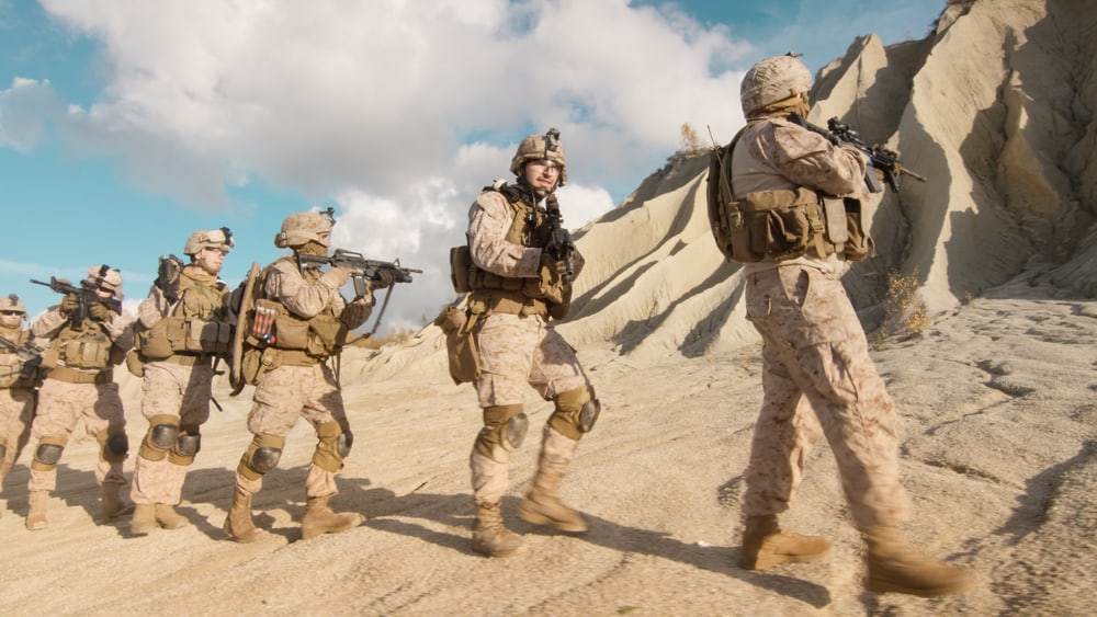 A squad of fully equipped and armed soldiers walking in single file in the desert.