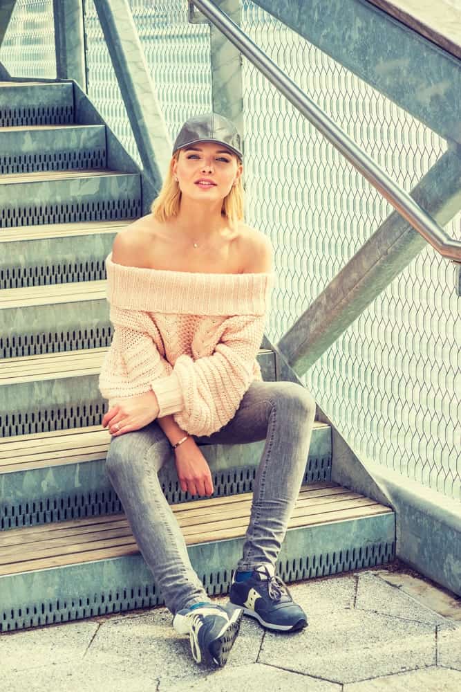 Woman sitting on stairs wearing an off-the-shoulder sweater.