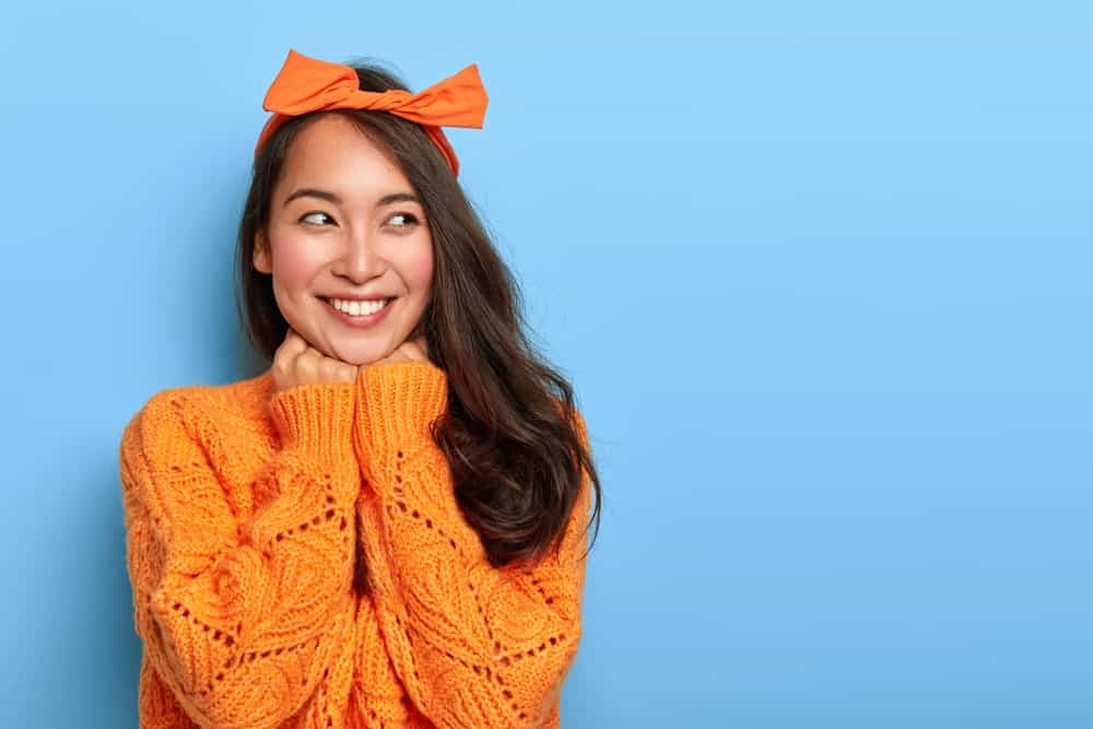 Smiling woman wearing an open knit sweater in bright orange with matching bow headband.
