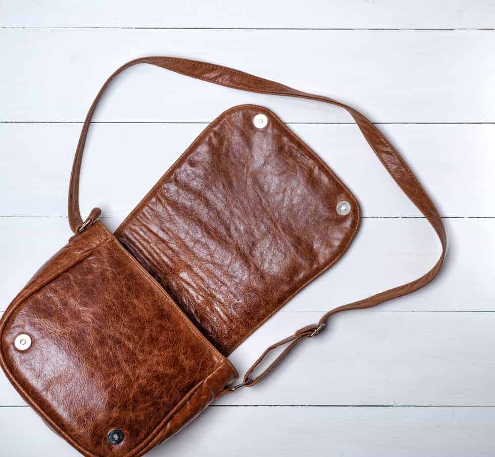 Brown leather saddle bag on a white wood plank background.