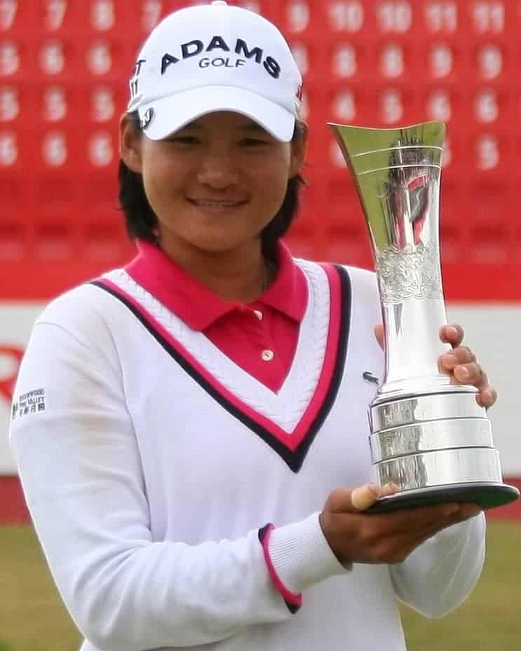 Woman in a white tennis sweater holding a gold trophy.