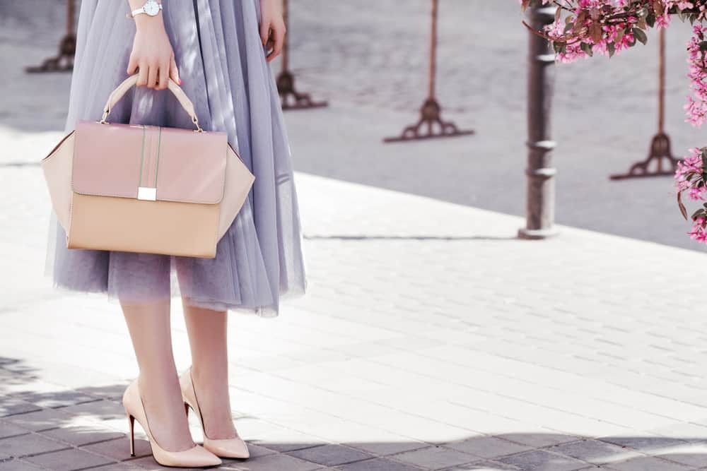 Woman in street holding a pink trapezoid handbag.