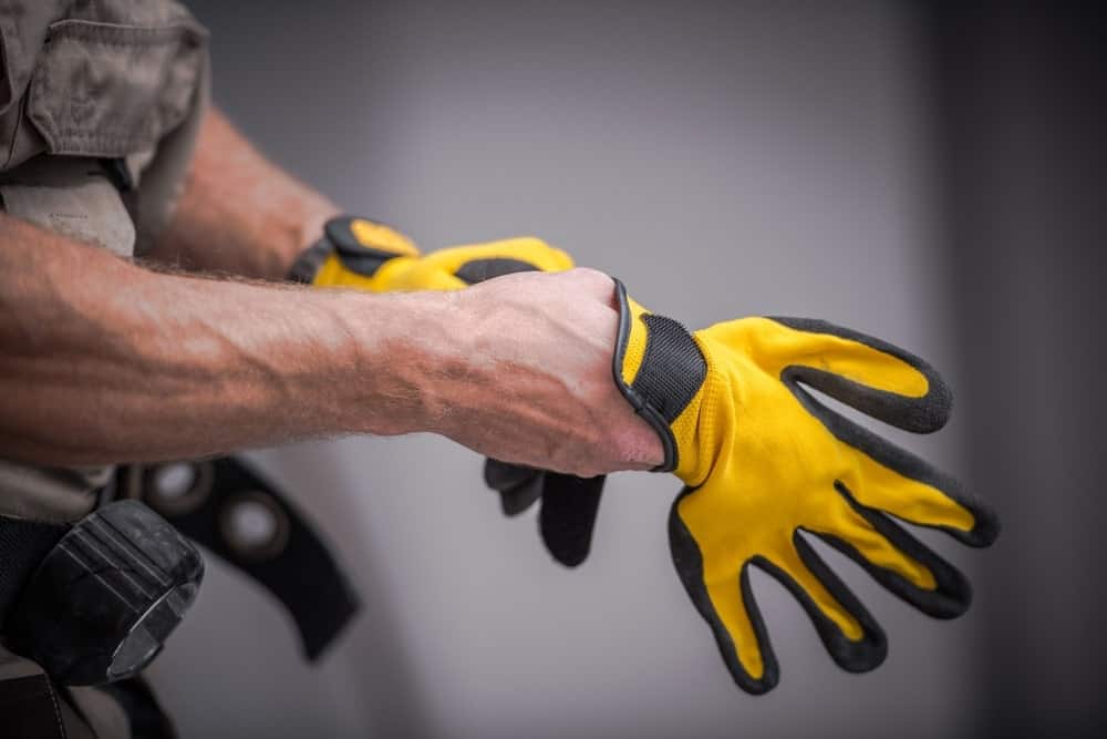 A man putting a pair of yellow utility gloves.