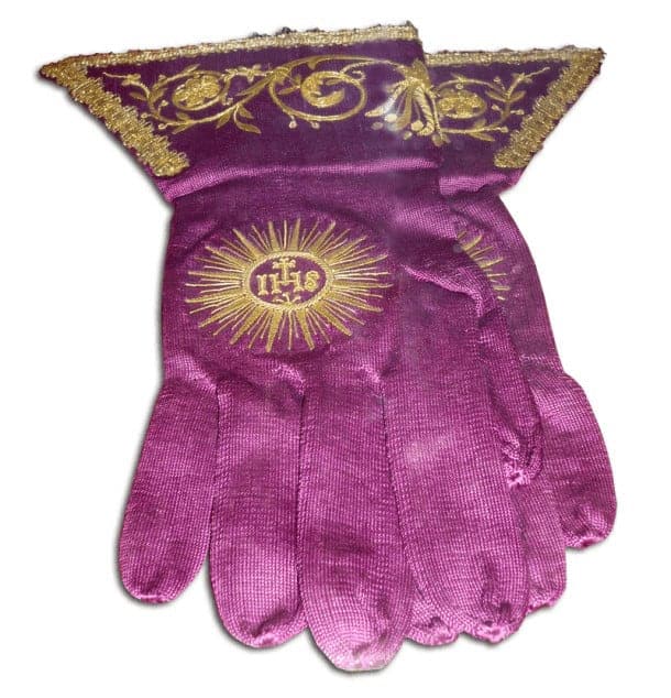 A pair of pink gloves with religious iconography embroidered on it.