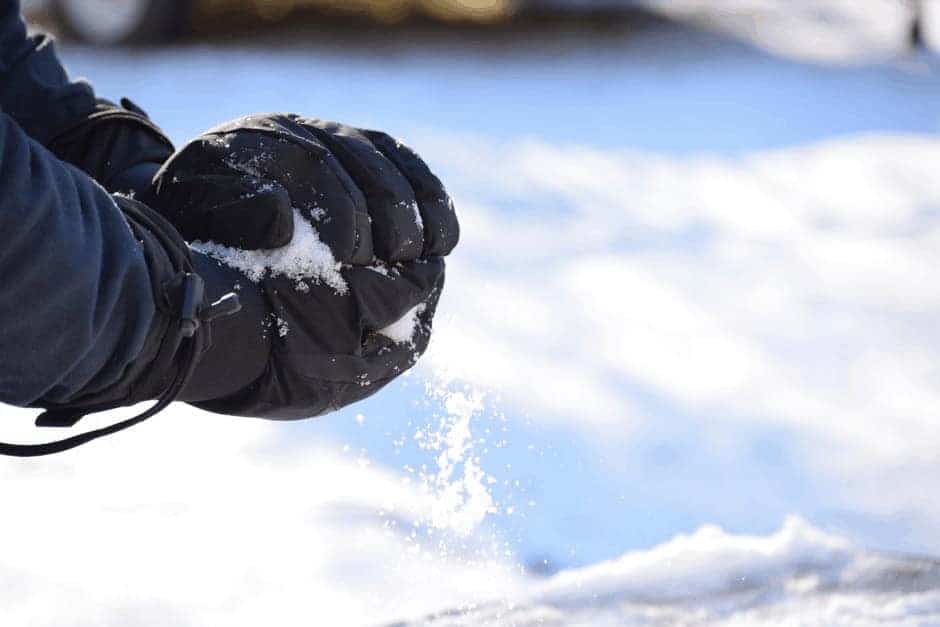 Gloved hands shaping some snow into a ball.