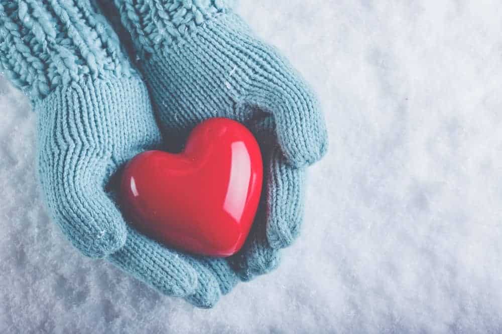 A pair of warm gloved hands holding a plastic heart.