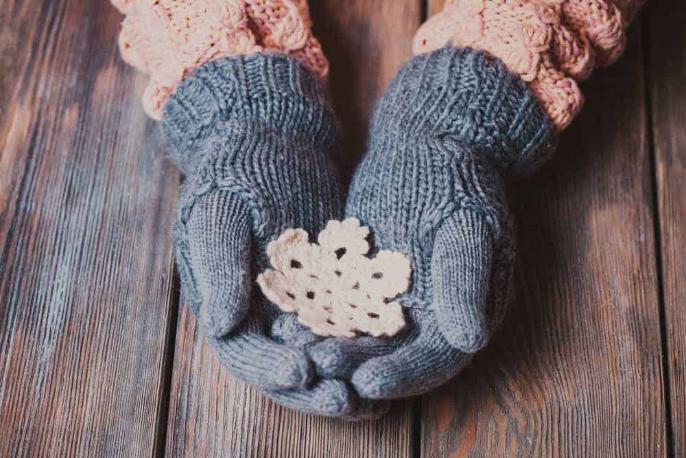 A warm and comfortable pair of knit Christmas gloves holding a knit snowflake.