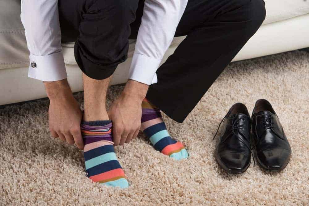 A man putting on a pair of colorful, striped socks.