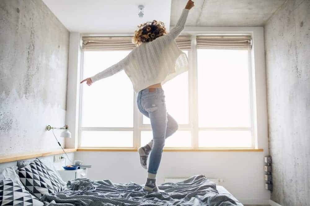 Woman in white sweater jumping on bed.