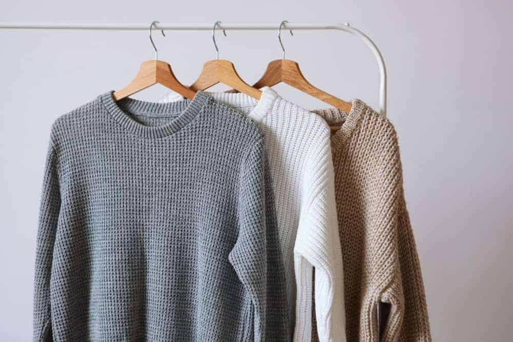 Warm sweaters hanging on a white rack.