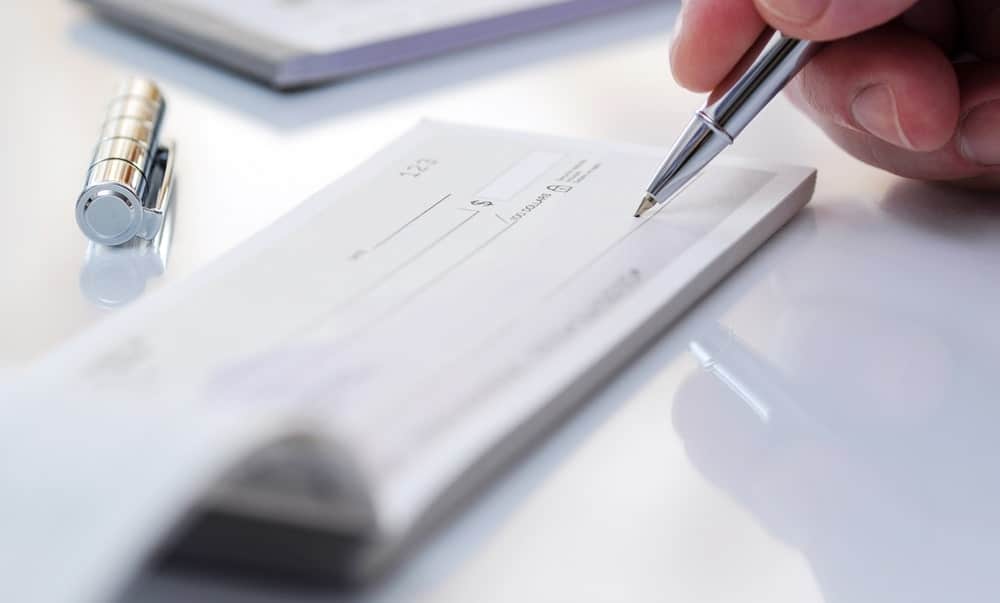 A close look at a person writing a check with the use of a check-safe pen.