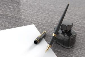 Fountain pen with pot of ink and blank page on a gray background