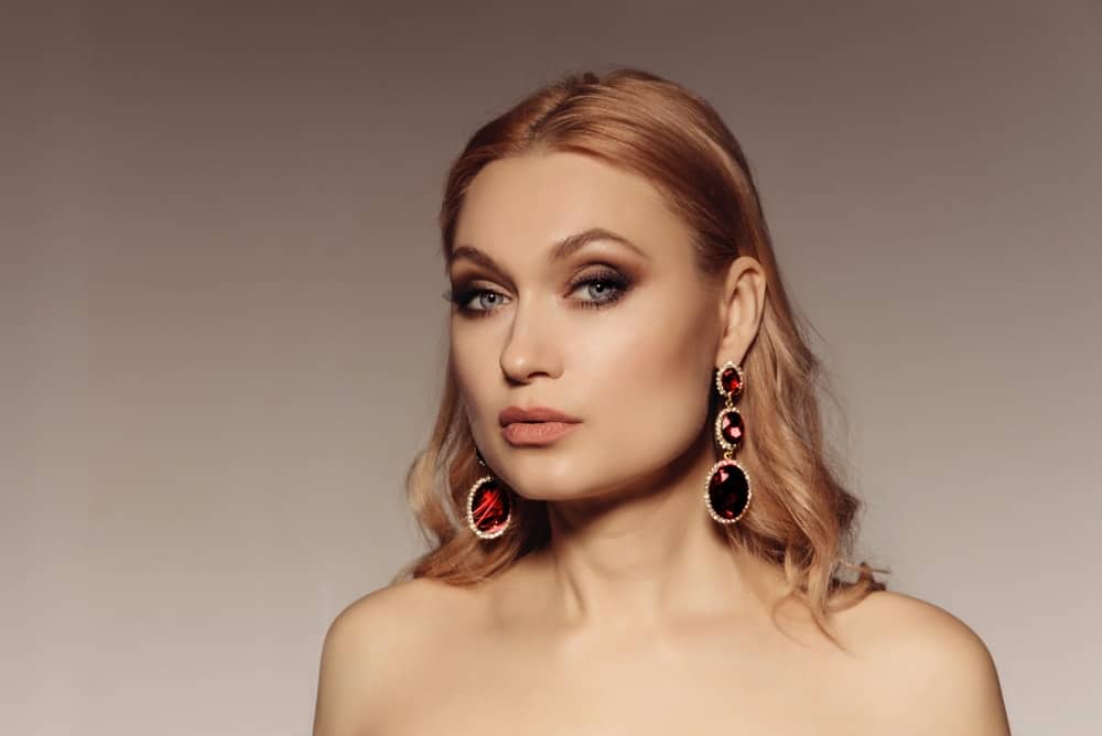 A blonde woman wearing a pair of ruby statement earrings.