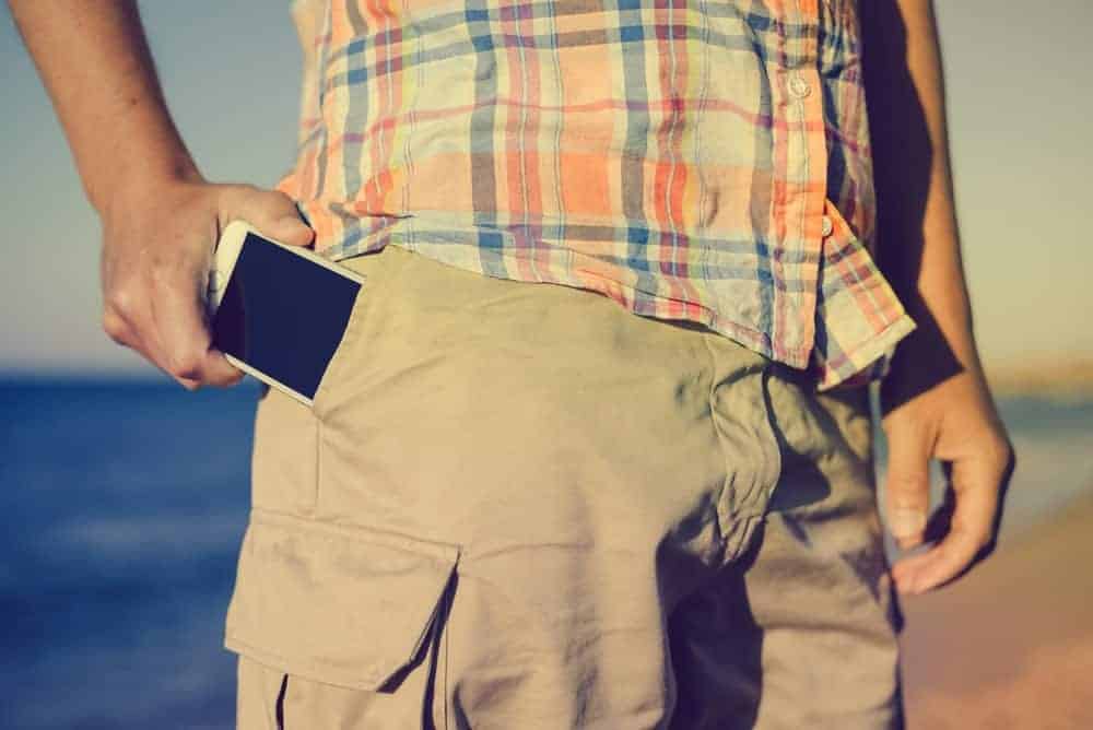 A close look at a man putting his phone into the pocket of his cargo shorts.