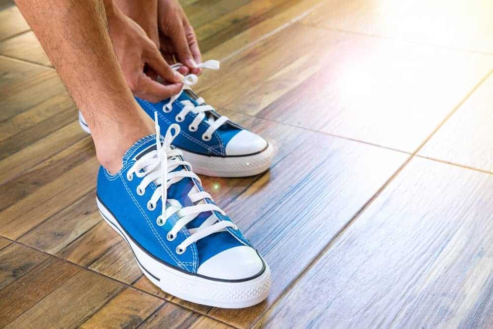 A man putting on his blue canvas sneakers.