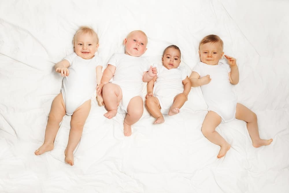 A row of four babies wearing white onesies.