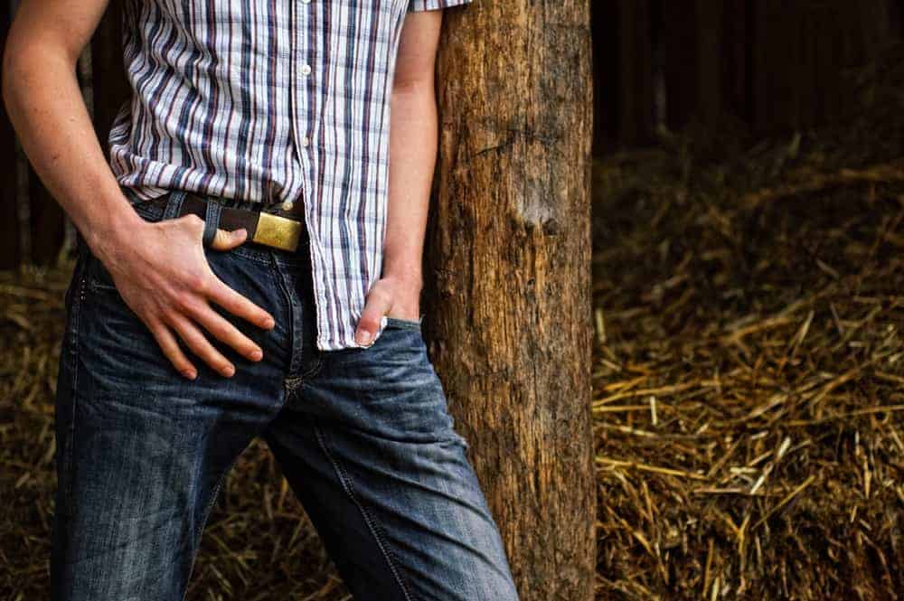 A man wearing cowboy jeans leaning on a tree.
