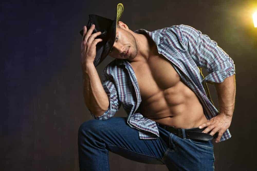 A man wearing cowboy jeans, button-down shirt and cowboy hat.
