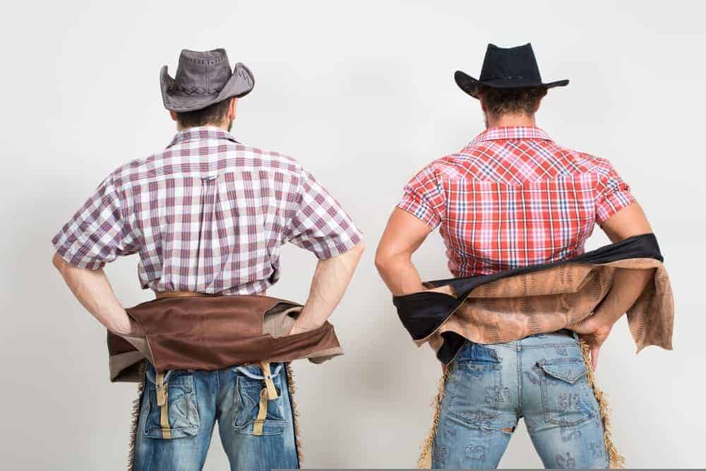 Two cowboys wearing jeans seen from behind.