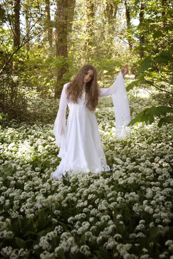 Woman in a forest wearing a white bell sleeve dress.