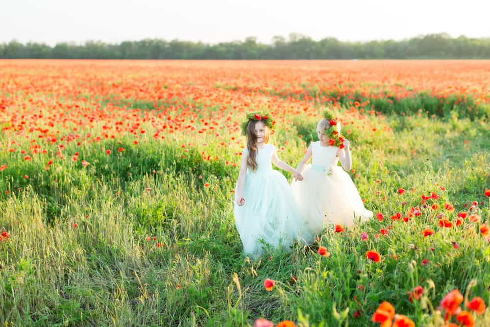 Two kids in a field wearing white dress and wreaths.