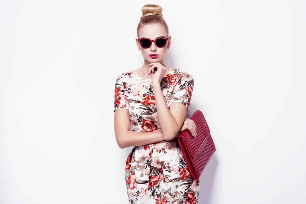 Model wearing a floral spring dress, sunglasses, and red purse.