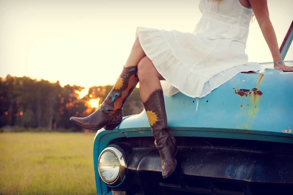 Woman in white dress and boots sitting on a blue truck.