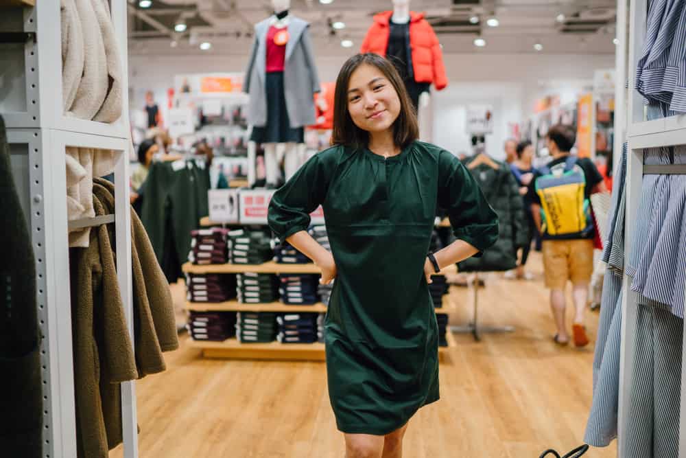 A woman tries on a green smock dress in a fashion store.