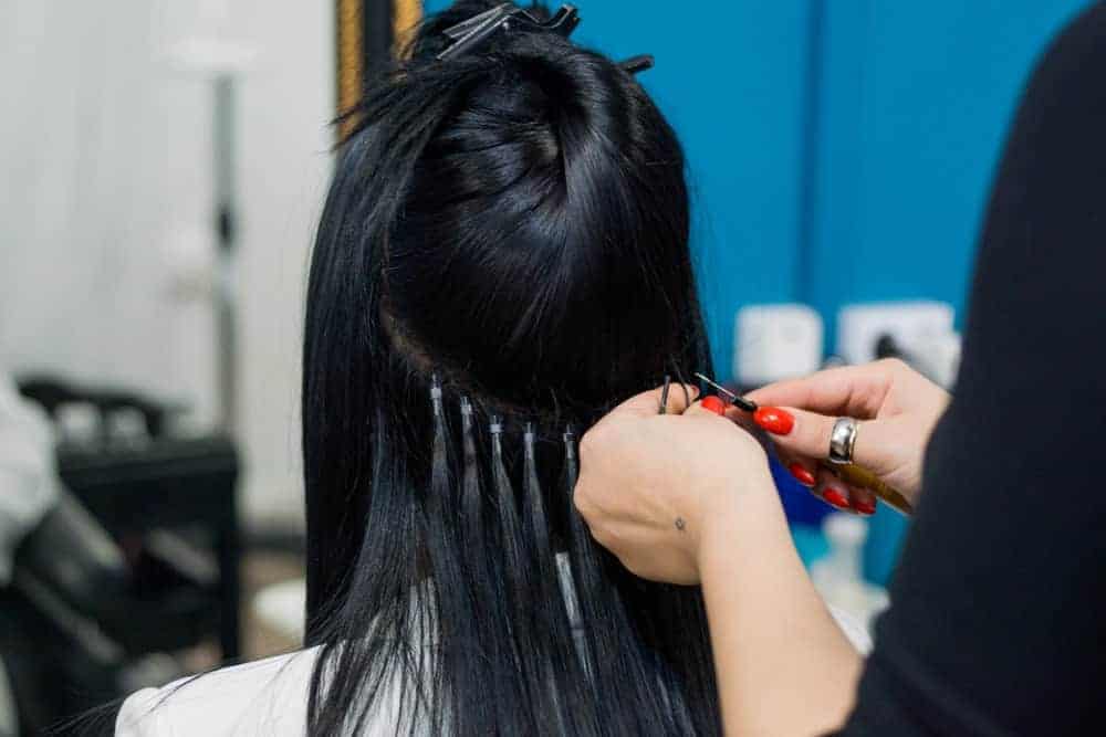 Stylist applying hair extensions to a woman's black hair.