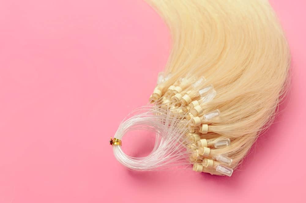 Pre-bonded straight flat human hair extensions against a pink background.