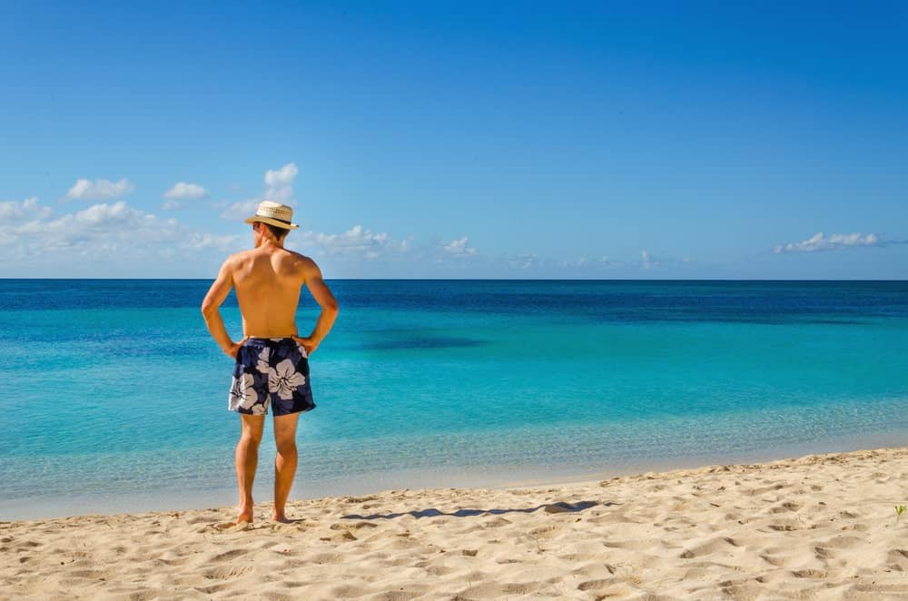 A man wearing a pair of floral swimming trunks at the beach.