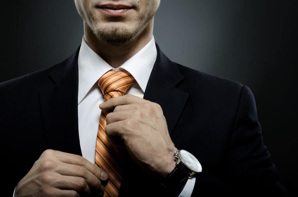 Man in black suit holding his orange striped necktie.