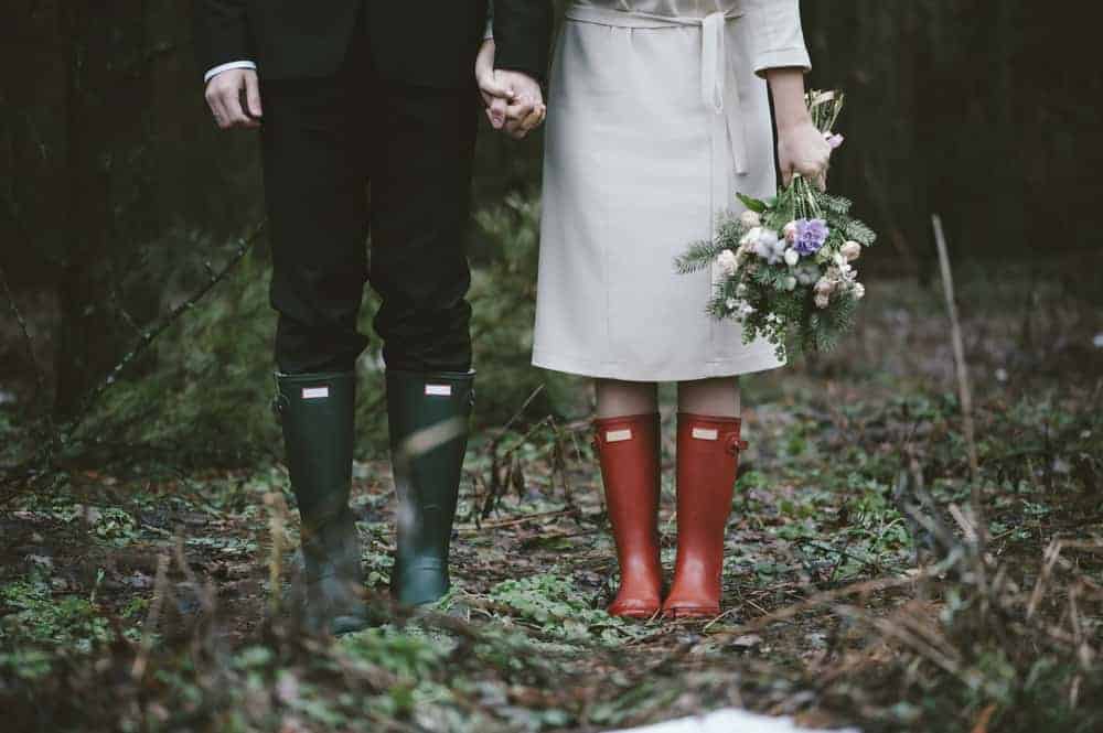 A couple in the middle of a forest wearing green and red boots.