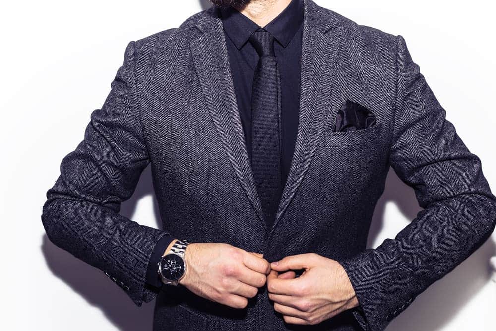 A close look at a man buttoning his charcoal black suit.