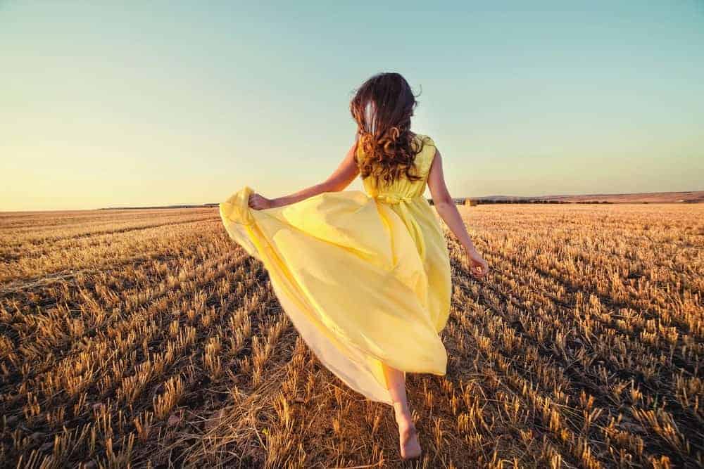 A woman running through the field wearing a buttercream yellow summer dress.