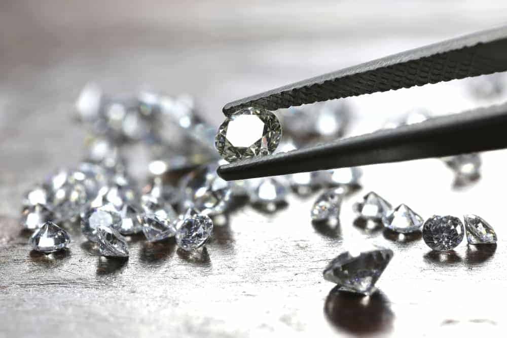 A close look at a pair of tweezers picking out one of the bunch of cut diamonds.