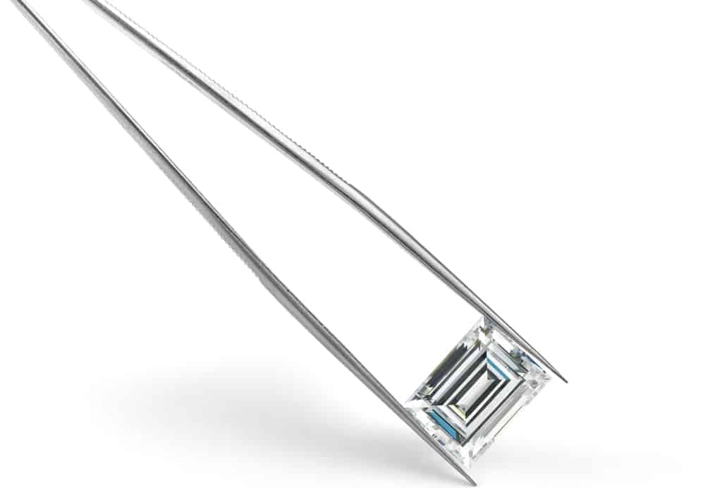A close look at a pair of tweezers holding a baguette cut diamond.