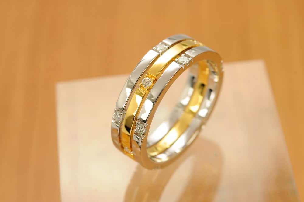 A two-tone band ring with diamonds on a wooden surface.